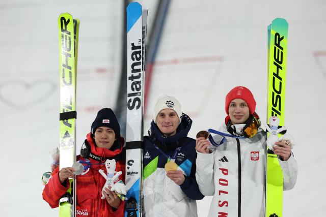(From L) Silver medallist Japan's Ren Nikaido, gold medallist Slovenia's Domen Prevc and bronze medallist Poland's Kacper Tomasiak celebrate on the podium of the men's large hill individual ski jumping of the Milano Cortina 2026 Winter Olympic Games at Predazzo Ski Jumping Stadium in Predazzo (Val di Fiemme), on February 14, 2026. (Photo by Anne-Christine POUJOULAT / AFP)