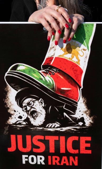 A female demonstrator holds a placard depicting the Supreme Leader of Iran Ayatollah Ali Khamenei being stepped on by a boot with an image of the pre-Islamic revolution of 1979 Iranian flag during a march in support of the people of Iran by members of the American-Iranian community in Washington, DC, on February 14, 2026. The demonstration comes after the bloody crackdown on protesters last month, while US President Donald Trump has been massing warships in the Middle East and declared Friday that a change of government in Iran would be the "best thing that could happen". (Photo by ROBERTO SCHMIDT / AFP)