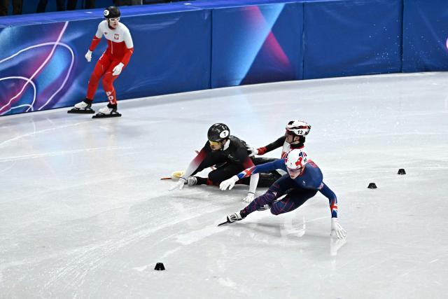 Canada's Felix Roussel (C) and Latvia's Roberts Kruzbergs (L) fall next to Britain's Niall Treacy while competing in the short track speed skating men's 1500m semi-final during the Milano Cortina 2026 Winter Olympic Games at Milano Ice Skating Arena in Milan on February 14, 2026. (Photo by Gabriel BOUYS / AFP)
