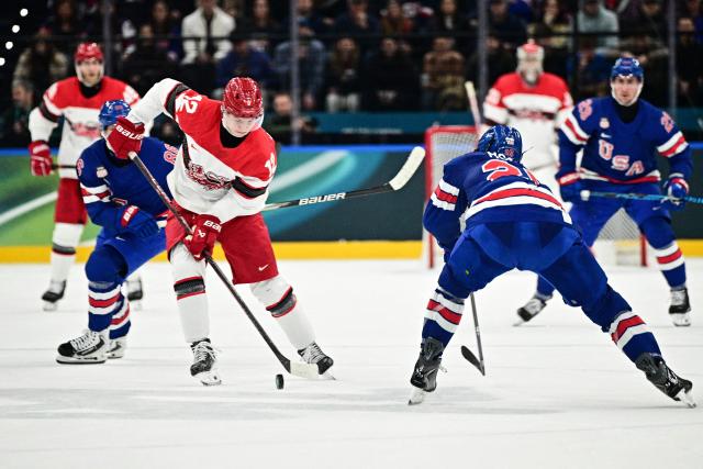 Denmark's #12 Oscar Moelgaard and USA's #25 Charlie McAvoy vie for the puck during the men's preliminary round Group C Ice Hockey match between USA and Denmark at the Milano Santagiulia Ice Hockey Arena during the Milano Cortina 2026 Winter Olympic Games in Milan, on February 14, 2026. (Photo by JULIEN DE ROSA / AFP)