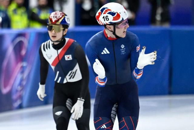 Britain's Niall Treacy reacts next to South Korea's Shin Dong-min after competing in the short track speed skating men's 1500m semi-final during the Milano Cortina 2026 Winter Olympic Games at Milano Ice Skating Arena in Milan on February 14, 2026. (Photo by WANG Zhao / AFP)