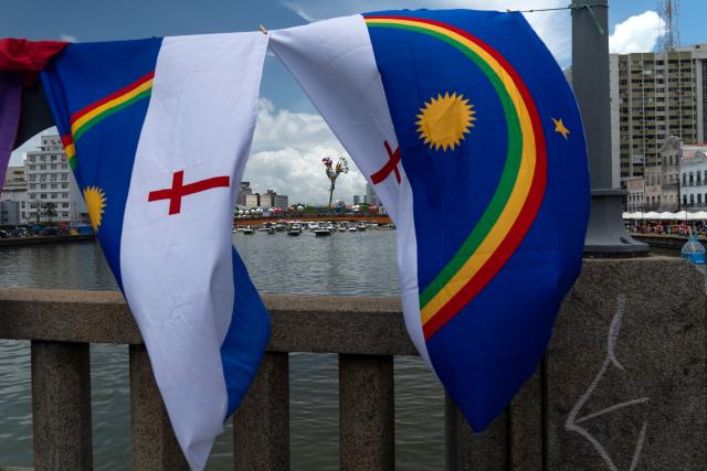 Flags of Pernambuco hang on a bridge as revelers take part in the Galo da Madrugada (Dawn Rooster) carnival band parade on the streets of Recife, Brazil on February 14, 2026. (Photo by Carlos FABAL / AFP)