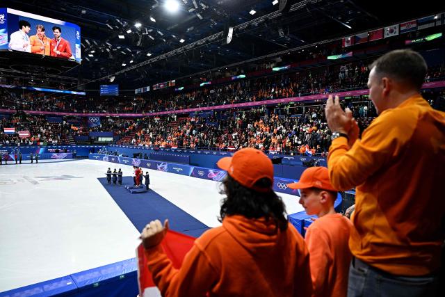 Fans watch a giant screen displaying (L-R) Silver medallist South Korea's Hwang Dae-heon, gold medallist Netherlands' Jens van 't Wout and bronze medallist Latvia's Roberts Kruzbergs during the victory ceremony of the short track speed skating men's 1500m final during the Milano Cortina 2026 Winter Olympic Games at Milano Ice Skating Arena in Milan on February 14, 2026. (Photo by Gabriel BOUYS / AFP)