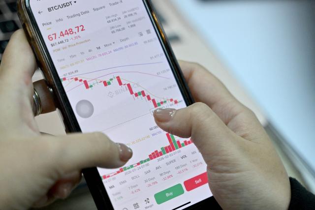 This photo taken on February 12, 2026 shows a Vietnamese cryptocurrency investor looking at the latest Bitcoin values on a smartphone in Hanoi. As a first-year computer science student in Hanoi, Hoang Le started trading crypto from his university dorm room, egged on by his gamer friends who were making a killing, and at one point his digital holdings swelled to $200,000 -- around 50 times the average annual income in Vietnam. But they crashed to zero when the bottom fell out of bitcoin and other cryptocurrencies in recent months. (Photo by Nhac NGUYEN / AFP) / To go with 'VIETNAM-ECONOMY-CRYPTO,FOCUS' by Lam NGUYEN