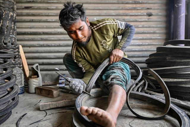 A worker cuts discarded tyres into strips for reuse at a small workshop in Dhaka on February 15, 2026. (Photo by Munir UZ ZAMAN / AFP)