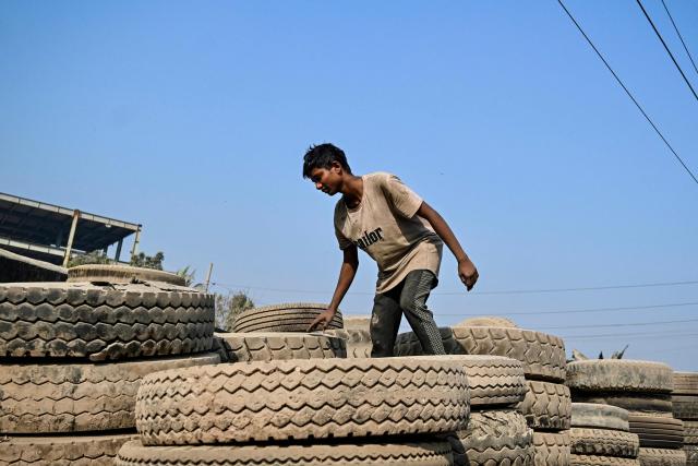 A worker sorts discarded tyres at a recycling yard in Dhaka on February 15, 2026. (Photo by Munir UZ ZAMAN / AFP)
