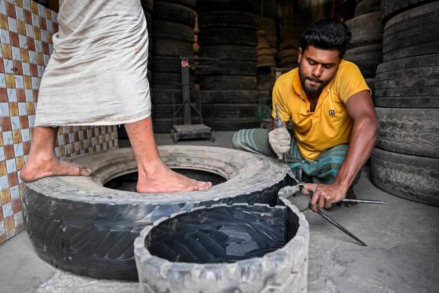 A worker cuts discarded tyres into strips for reuse at a small workshop in Dhaka on February 15, 2026. (Photo by Munir UZ ZAMAN / AFP)