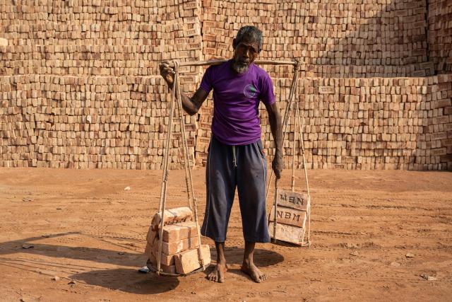 A Bangladeshi man carrying bricks poses for a photograph in Dhaka on February 15, 2026. (Photo by Mohd RASFAN / AFP)