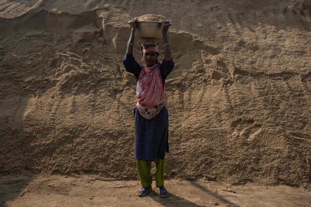 A Bangladeshi woman poses for a photograph with a bucket of sand on her head in Dhaka on February 15, 2026. (Photo by Mohd RASFAN / AFP)