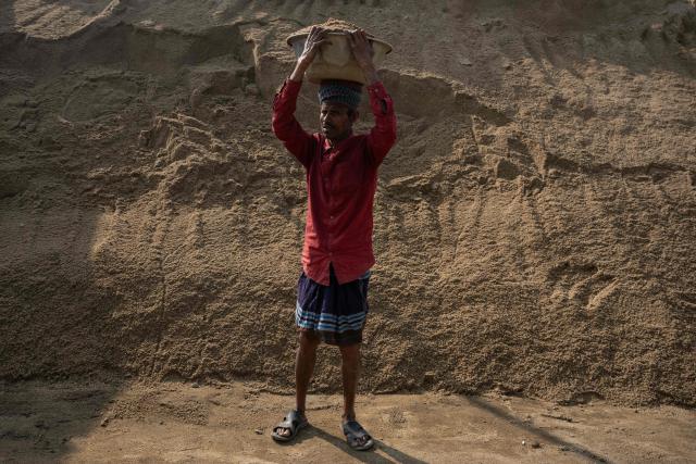A Bangladeshi man poses for a photograph with a bucket of sand on his head in Dhaka on February 15, 2026. (Photo by Mohd RASFAN / AFP)