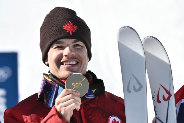 Gold medallist Canada's Mikael Kingsbury celebrates on the podium after the freestyle skiing men's dual moguls final during the Milano Cortina 2026 Winter Olympic Games at Livigno Aerials & Moguls Park, in Livigno (Valtellina), on February 15, 2026. (Photo by Jeff PACHOUD / AFP)
