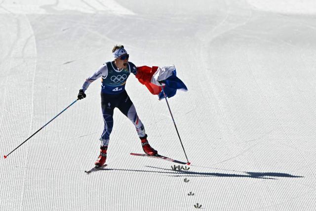 France's Victor Lovera celebrates with a French flag as he skies tot he finish line during the cross-country men's 4 x 7,5km relay event of the Milano Cortina 2026 Winter Olympic Games at Tesero Cross-Country Skiing Stadium in Lago di Tesero (Val di Fiemme), on February 15, 2026. (Photo by Javier SORIANO / AFP)