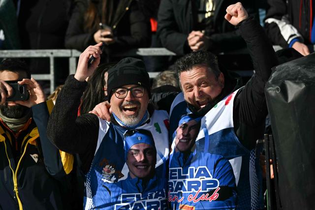 Italian fans with shirts displaying the portait of Italy's Elia Barp gestures as they attend the cross-country men's 4 x 7,5km relay event of the Milano Cortina 2026 Winter Olympic Games at Tesero Cross-Country Skiing Stadium in Lago di Tesero (Val di Fiemme), on February 15, 2026. (Photo by Javier SORIANO / AFP)