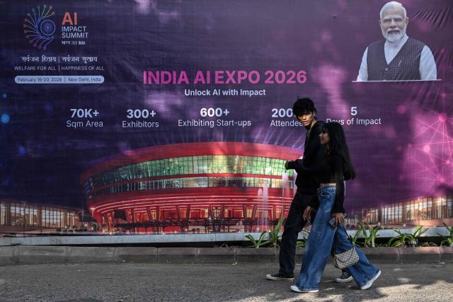 Commuters walk past a hoarding of the AI Expo along a street on the eve of the 'India AI Impact Summit 2026' in New Delhi on February 15, 2026. (Photo by Arun SANKAR / AFP)