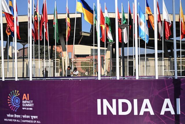 Workers install the national flags of participating countries on the eve of the 'India AI Impact Summit 2026' at the Bharat Mandapam in New Delhi on February 15, 2026. (Photo by Arun SANKAR / AFP)