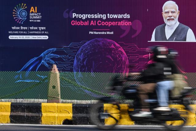 A motorcyclist rides past the hoarding of 'India AI Impact Summit 2026' along a street on the eve of the summit in New Delhi on February 15, 2026. (Photo by Arun SANKAR / AFP)