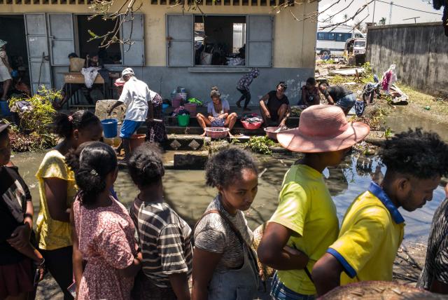 TOPSHOT - Residents wash their clothes as other queue during a food distribution at a public primary school used as a shelter for people affected by the passage of tropical cyclone Gezani during the night of February 10 to 11, in Toamasina on February 15, 2026. (Photo by RIJASOLO / AFP)