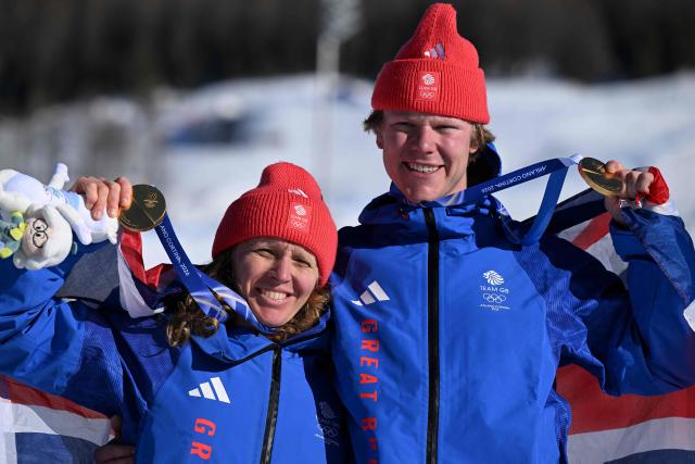 Gold medallists Britain's Charlotte Bankes and Huw Nightingale pose on the podium after the snowboard mixed team cross final during the Milano Cortina 2026 Winter Olympic Games at Livigno Snow Park, in Livigno (Valtellina), on February 15, 2026. (Photo by Kirill KUDRYAVTSEV / AFP)