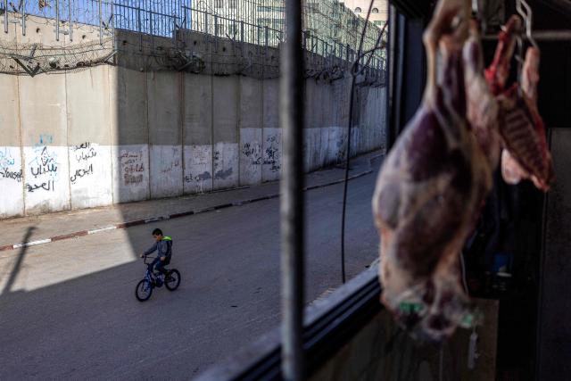 A Palestinian boy cycles outside a butcher's shop near Israel's controversial separation barrier in the Dahiat al-Barit suburb of east Jerusalem on February 15, 2026. (Photo by Ilia YEFIMOVICH / AFP)