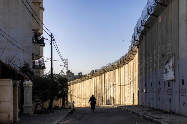 TOPSHOT - A Palestinian woman walks next to Israel's controversial separation barrier in the Dahiat al-Barit suburb of east Jerusalem on February 15, 2026. (Photo by Ilia YEFIMOVICH / AFP)