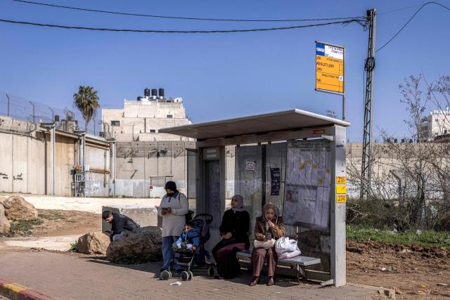 Palestinian women wait for a bus at a stop near Israel's controversial separation barrier in the Dahiat al-Barit suburb of east Jerusalem on February 15, 2026. (Photo by Ilia YEFIMOVICH / AFP)