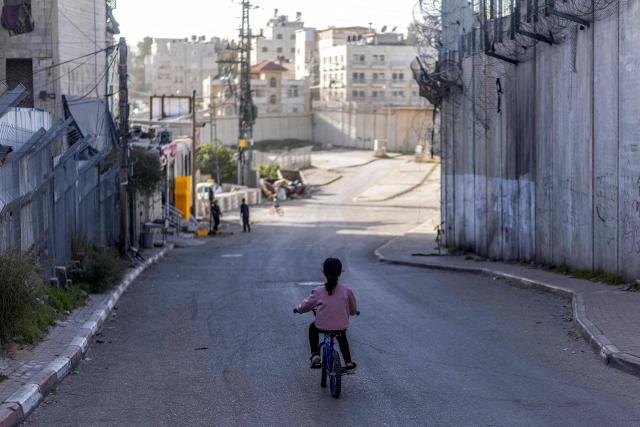 A Palestinian child rides a bicycle near police barriers preventing vehicles from entering the area and next to Israel's controversial separation barrier in the Dahiat al-Barit suburb of east Jerusalem on February 15, 2026. (Photo by Ilia YEFIMOVICH / AFP)