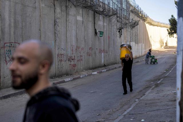 Palestinian men walk next to Israel's controversial separation barrier in the Dahiat al-Barit suburb of east Jerusalem on February 15, 2026. (Photo by Ilia YEFIMOVICH / AFP)