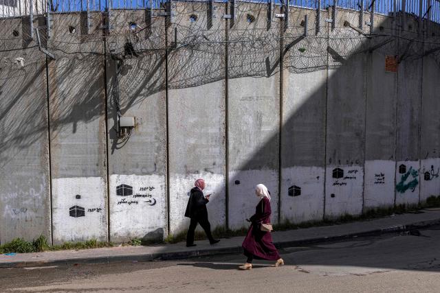 Palestinian women walk next to Israel's controversial separation barrier in the Dahiat al-Barit suburb of east Jerusalem on February 15, 2026. (Photo by Ilia YEFIMOVICH / AFP)