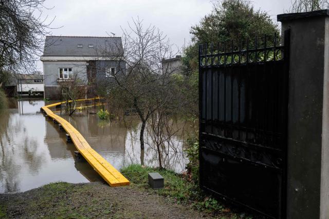 This photograph shows a temporary walkway leading to a house surrounded by flood water in Pont de Ce, western France, on February 15, 2026. The prefecture of Maine-et-Loire issued an evacuation order on the evening of February 14, 2026 evening for several municipalities near Angers which were deemed to be at risk of being isolated by floods and flooded roads. (Photo by Sebastien Salom-Gomis / AFP)