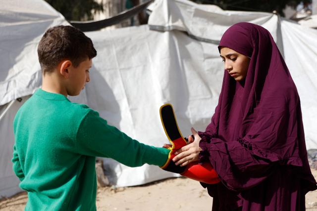 Displaced Palestinian amateur boxer, 18-year-old Farah Abu Al-Qumsan (R), adjusts the gloves of a boy as she leads a boxing training session for youths amid tents in Gaza City on February 15, 2026. A US-brokered ceasefire, which sought to halt the fighting between Israel and Hamas sparked by the group's October 2023 attack, took effect last October, reducing the level of bombing and fighting in the Gaza Strip. (Photo by Omar AL-QATTAA / AFP)