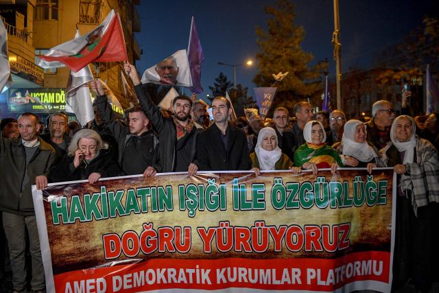 Members of the Kurdish community hold a banner reading "We are walking towards freedom with the light of truth" as they take part in a protest calling for the release of convicted Kurdistan Worker's Party (PKK) leader Abdullah Ocalan in Diyarbakir on February 15, 2026. Ocalan was captured by Turkish secret agents in Kenya in 1999, brought to Turkey and sentenced to death. His sentence was later commuted to life imprisonment. (Photo by Ilyas AKENGIN / AFP)
