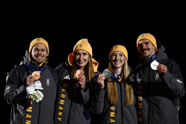 (From L) Bronze medallists Germany's Christopher Grotheer and Germany's Jacqueline Pfeifer, and silver medallists Germany's Susanne Kreher and Germany's Axel Jungk celebrate on the podium after competing in the skeleton mixed team event at Cortina Sliding Centre during the Milano Cortina 2026 Winter Olympic Games in Cortina d'Ampezzo on February 15, 2026. (Photo by Marco BERTORELLO / AFP)