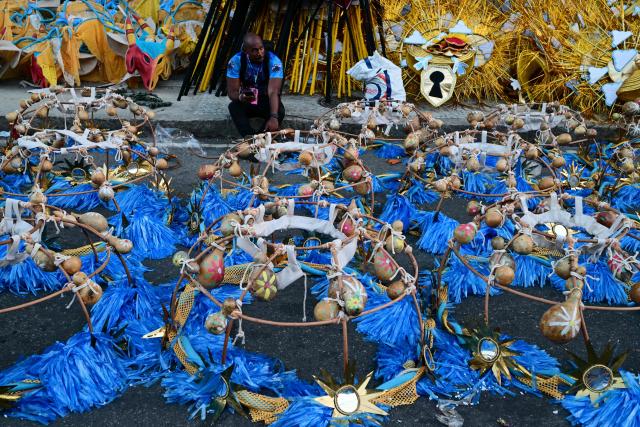 A man rests in front of costumes of the revellers of the Academicos de Niteroi samba school before the opening night of the Rio Carnival at the Marques de Sapucai Sambadrome in Rio de Janeiro, Brazil, on February 15, 2026. (Photo by Pablo PORCIUNCULA / AFP)