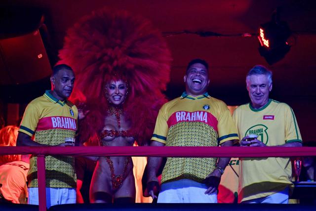 Brazil's Italian national football team coach Carlo Ancelotti (R), former football players Ronaldo (C-R) and Denilson (L) smile above a float of the Academicos de Niteroi samba school before the opening night of the Rio Carnival at the Marques de Sapucai Sambadrome in Rio de Janeiro, Brazil, on February 15, 2026. (Photo by Pablo PORCIUNCULA / AFP)
