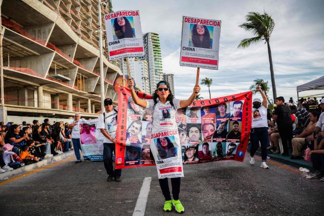 A member of a group of "searching mothers" holds portraits of a missing person during the parade of International Carnival in Mazatlan, Sinaloa State, Mexico, on February 15, 2026. (Photo by Jesus Verdugo / AFP)