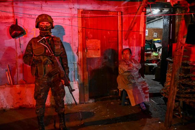 (FILES) A Guatemalan Army soldier stands guard next to an elderly woman on a street of the Gallito neighborhood during the state of emergency declared by the government in Guatemala City on January 22, 2026. Guatemalan President Bernardo Arevalo said on February 15, 2026, that the state of emergency he declared a month ago, which ends on February 16, had helped to control the gangs that killed eleven police officers in January and rioted in prisons. (Photo by JOHAN ORDONEZ / AFP)