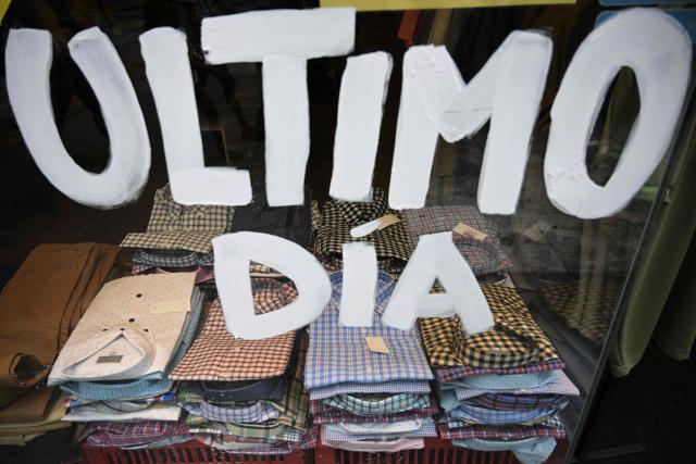 Short-sleeved shirts for sale are displayed in a shop window painted with the phrase "Last Day" in Buenos Aires on February 9, 2026. The textile industry in Argentina is going through a crisis with falling sales, rising local production costs, and concerns about competition from imports. Since 2023, the textile sector has laid off more than 18,000 people and is operating at one-third of its installed capacity, according to February data from the consulting firm Analytica and the Argentine Textile Industries Federation (FITA). (Photo by JUAN MABROMATA / AFP)
