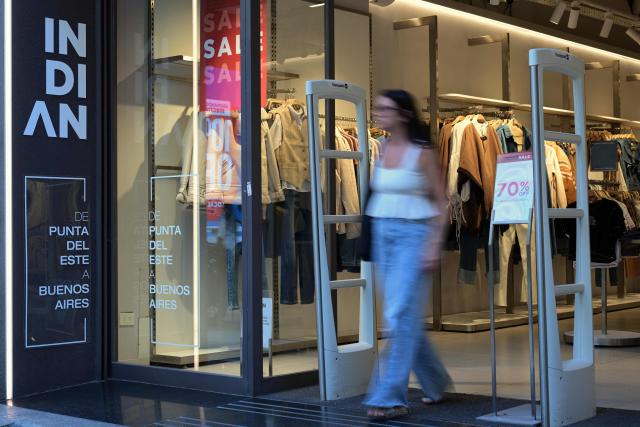 A woman leaves a shop with imported clothes in Buenos Aires on February 6, 2026. The textile industry in Argentina is going through a crisis with falling sales, rising local production costs, and concerns about competition from imports. Since 2023, the textile sector has laid off more than 18,000 people and is operating at one-third of its installed capacity, according to February data from the consulting firm Analytica and the Argentine Textile Industries Federation (FITA). (Photo by JUAN MABROMATA / AFP)
