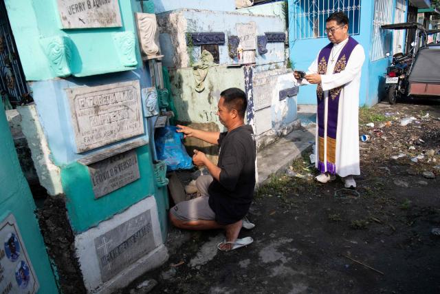 Roman Catholic priest Father Flavie Villanueva (R) takes photos as a worker removes the remains of Edward Sentorias, a victim of former Philippine president Rodrigo Duterte's war on drugs, during an exhumation at a cemetery in Manila on February 16, 2026. The bones will be transferred to the University of the Philippines College of Medicine for examination. ICC prosecutors have charged Duterte with three counts of crimes against humanity, alleging his involvement in at least 76 murders between 2013 and 2018 as part of his "war on drugs". (Photo by Ted ALJIBE / AFP)