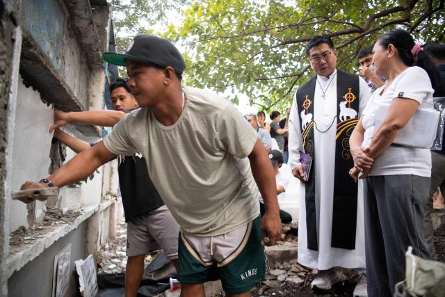 Roman Catholic priest Father Flavie Villanueva (R) talks to Mary Ann Pajo as they move the remains of her son Joewarski Pajo, a victim of former Philippine president Rodrigo Duterte's war on drugs, into a body bag during an exhumation at a cemetery in Manila on February 16, 2026. The bones will be transferred to the University of the Philippines College of Medicine for examination. ICC prosecutors have charged Duterte with three counts of crimes against humanity, alleging his involvement in at least 76 murders between 2013 and 2018 as part of his "war on drugs". (Photo by Ted ALJIBE / AFP)