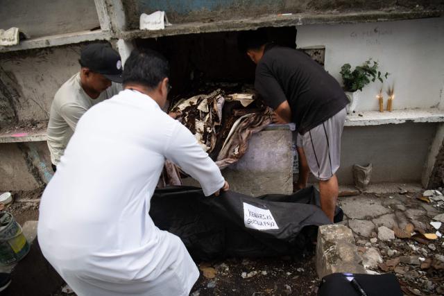 Roman Catholic priest Father Flavie Villanueva (C) helps workers remove the remains of Joewarski Pajo, a victim of former Philippine president Rodrigo Duterte's war on drugs, into a body bag during an exhumation at a cemetery in Manila on February 16, 2026. The bones will be transferred to the University of the Philippines College of Medicine for examination. ICC prosecutors have charged Duterte with three counts of crimes against humanity, alleging his involvement in at least 76 murders between 2013 and 2018 as part of his "war on drugs". (Photo by Ted ALJIBE / AFP)