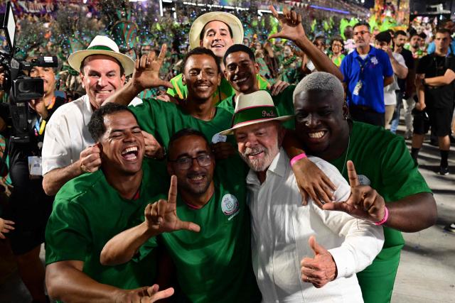 Brazil's President Luiz Inacio Lula da Silva (2nd R) and Rio de Janeiro's mayor Eduardo Paes (L) pose with revellers of the Mangueira samba school during the opening night of the Rio Carnival at the Marques de Sapucai Sambadrome in Rio de Janeiro on February 16, 2026. (Photo by Pablo PORCIUNCULA / AFP)