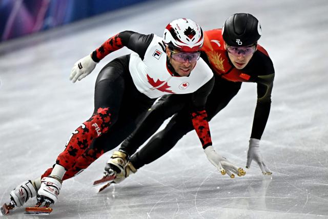Canada's William Dandjinou and China's Liu Shaoang compete in the short track speed skating men's 5000m relay semi-final during the Milano Cortina 2026 Winter Olympic Games at Milano Ice Skating Arena in Milan on February 16, 2026. (Photo by Gabriel BOUYS / AFP)