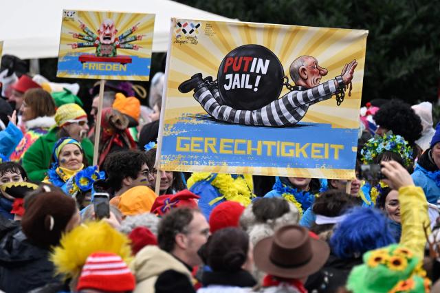 Revellers hold a placard depicting Russian President Vladimir Putin being handcuffs and the text reading:"Justice" during the parade to celebrate Rose Monday (Rosenmontag), on February 16, 2026 in Duesseldorf, western Germany. (Photo by INA FASSBENDER / AFP)
