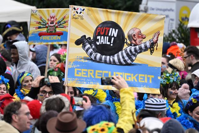 Revellers hold a placard depicting Russian President Vladimir Putin being handcuffs and the text reading:"Justice" during the parade to celebrate Rose Monday (Rosenmontag), on February 16, 2026 in Duesseldorf, western Germany. (Photo by INA FASSBENDER / AFP)