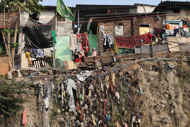 A woman sits outside a slum house, over a slope strewn with garbage in Mumbai on February 16, 2026. (Photo by Ludovic MARIN / AFP)