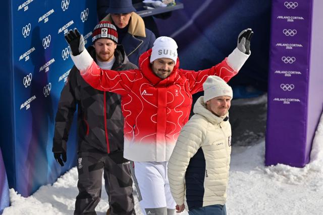 Gold medallist Switzerland's Loic Meillard (C), silver medallist Austria's Fabio Gstrein (L) and bronze medallist Norway's Henrik Kristoffersen (R) arrive for the podium ceremony of the men's slalom alpine skiing event during the Milano Cortina 2026 Winter Olympic Games at the Stelvio Ski Centre in Bormio (Valtellina) on February 16, 2026. (Photo by Fabrice COFFRINI / AFP)