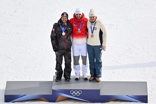 Gold medallist Switzerland's Loic Meillard (C), silver medallist Austria's Fabio Gstrein (L) and bronze medallist Norway's Henrik Kristoffersen (R) pose on the podium of the men's slalom alpine skiing event during the Milano Cortina 2026 Winter Olympic Games at the Stelvio Ski Centre in Bormio (Valtellina) on February 16, 2026. (Photo by Fabrice COFFRINI / AFP)