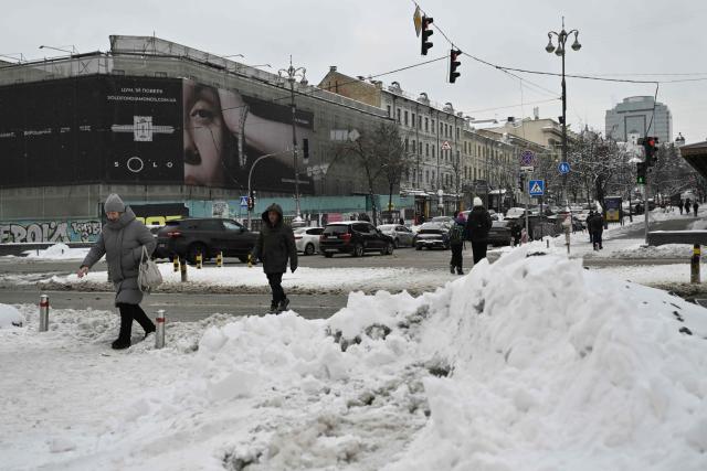Pedestrians cross a snow-covered road in central Kyiv following overnight snowfall on February 16, 2026, amid the Russian invasion of Ukraine. (Photo by Genya SAVILOV / AFP)