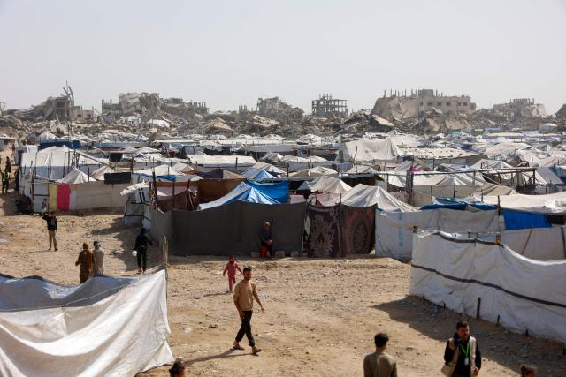 Palestinians walk next to shelters amid the rubble of destroyed buildings in Gaza City, on February 16, 2026. A US-brokered ceasefire, which sought to halt the fighting between Israel and Hamas sparked by the group's October 2023 attack, took effect last October, reducing the level of bombing and fighting in the Gaza Strip. (Photo by Omar AL-QATTAA / AFP)